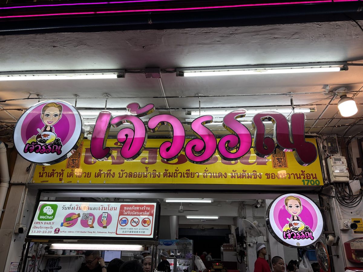 夜の食堂の店先。ピンクのネオン看板にタイ文字が光る