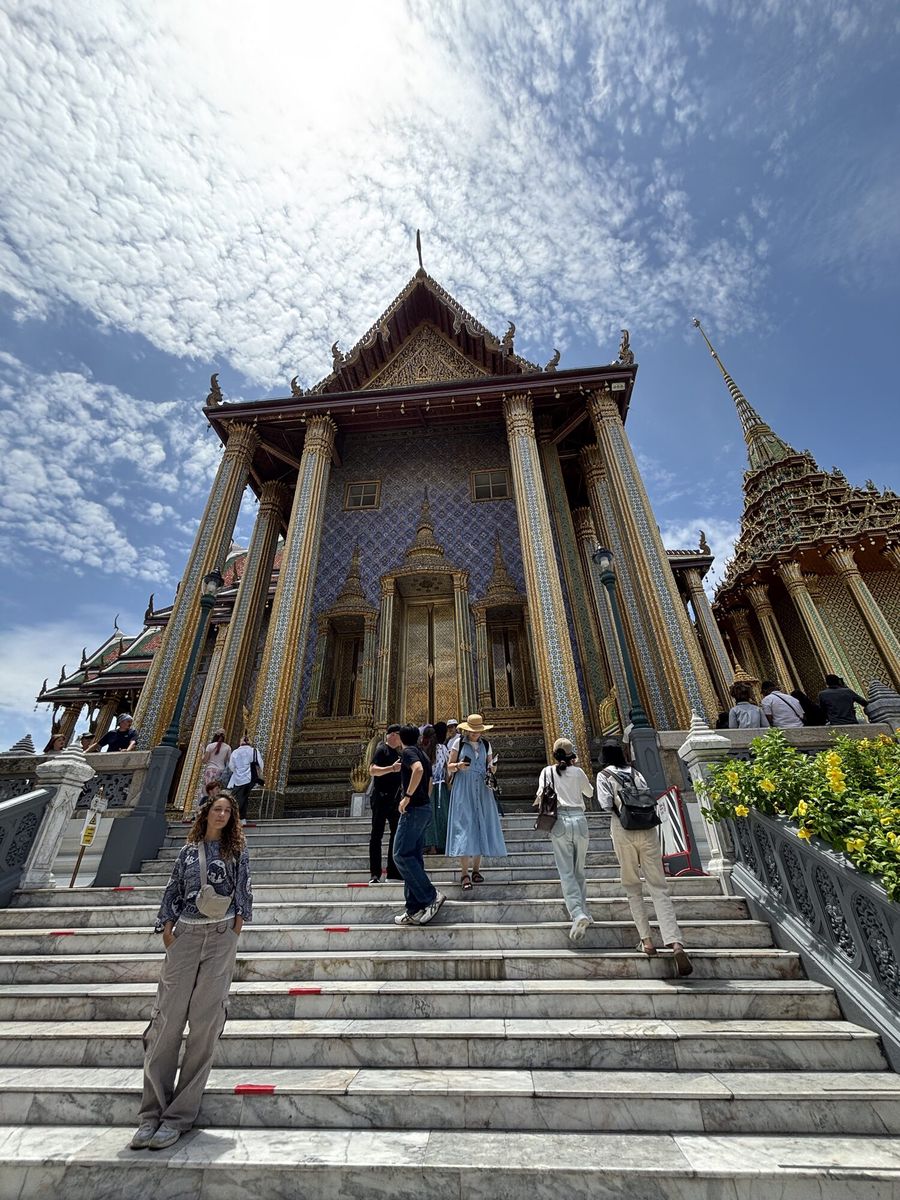 階段の上に建つ寺院の本堂。柱が立ち並び、右手に金色の仏塔が見える
