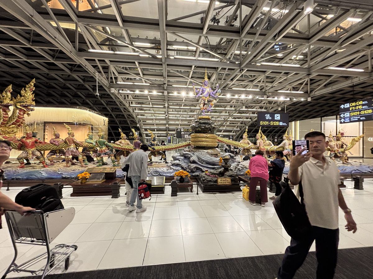 スワンナプーム空港の出発フロア。金色の装飾の前を旅行者が歩く